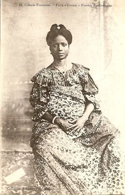 Woman from the African Coast photographed by F.W.H Arkhurst, with their hair swept high and adorned with gold ornament. Sourced from AdireAfricanTextiles.blogspot.com.