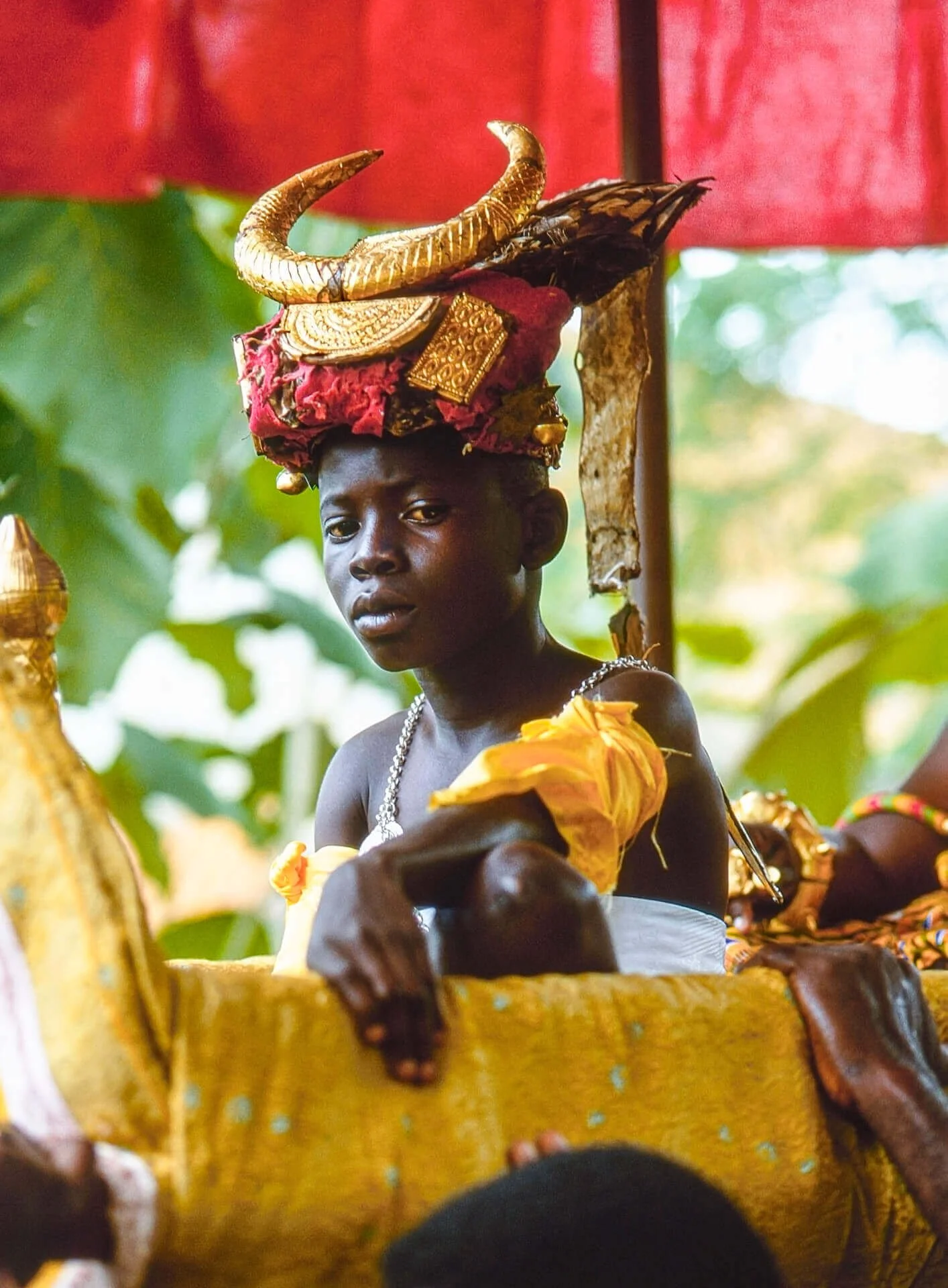 Ashanti Soul Bearer, Ghana. Unknown photographer. (n.d.). This image depicts a young Ashanti Soul Bearer, a sacred attendant tasked with protecting his chief from spiritual and physical harm. He wears a striking gilded ram’s horn headdress adorned wi