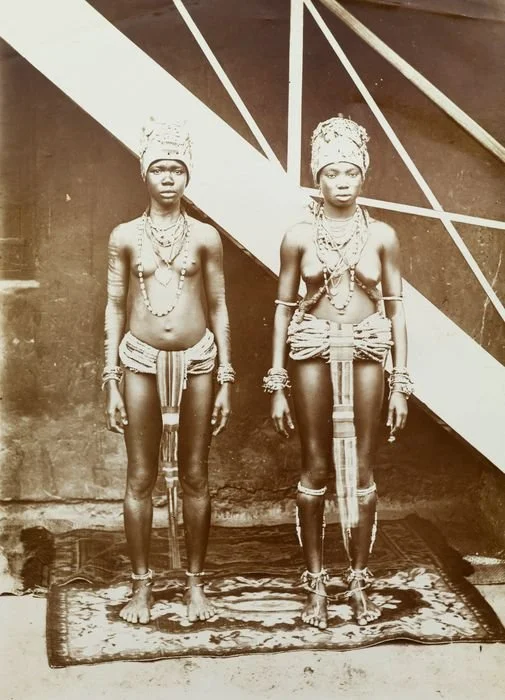 Portrait of two West African youths in ceremonial adornment, photographed during the colonial era, likely for ethnographic or exhibition purposes (British Empire & Commonwealth Collection). Unknown photographer. (c. early 20th century). Photograph of