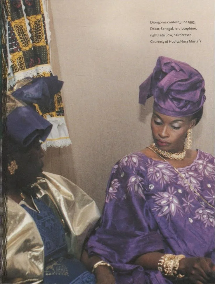 Senegalese women wearing indigo and violet boubous with headwraps and gold jewelry.