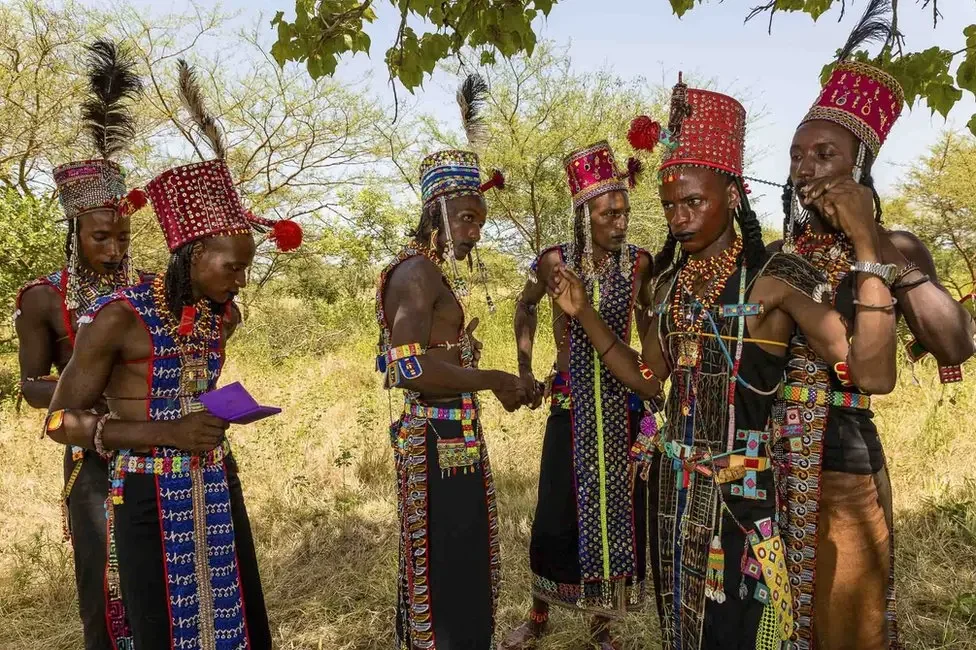 Wodaabe men make some last-minute adjustments to their costumes. By Tariq Zaidi. — Source: BBC