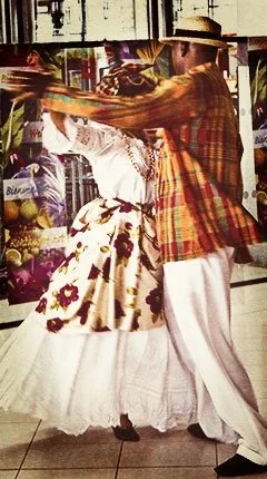 Martinican couple performing biguine in traditional Creole attire, including a madras headwrap, patterned skirt, and straw hat.