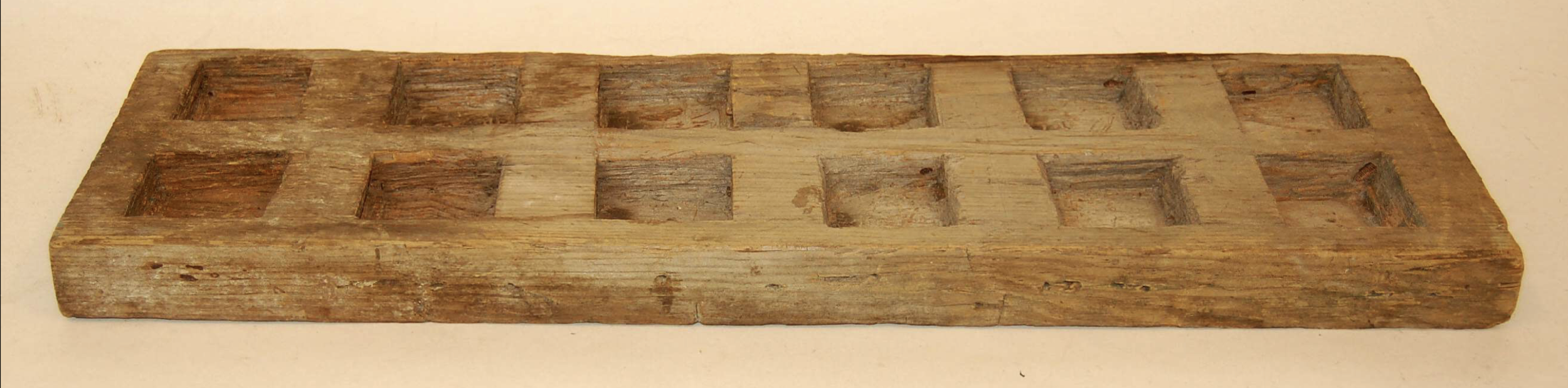 Warri-Board (Mancala Board). 1940s. Carved wood; Length 63.50 cm × Width 18.50 cm × Depth 4 cm. Speightstown, St Peter, Barbados (Lesser Antilles, Caribbean). This wooden warri-board is carved from a rectangular plank featuring twelve square, flat-bo