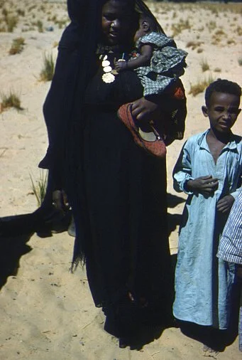 "Woman + child - Faras." A Nubian woman carrying her child with accompanying children in a desert landscape. Emery, J. (Photographer). (Woman + child - Faras). Flickr.  © James Emery. Licensed under the Creative Commons Attribution 2.0 Generic (CC BY