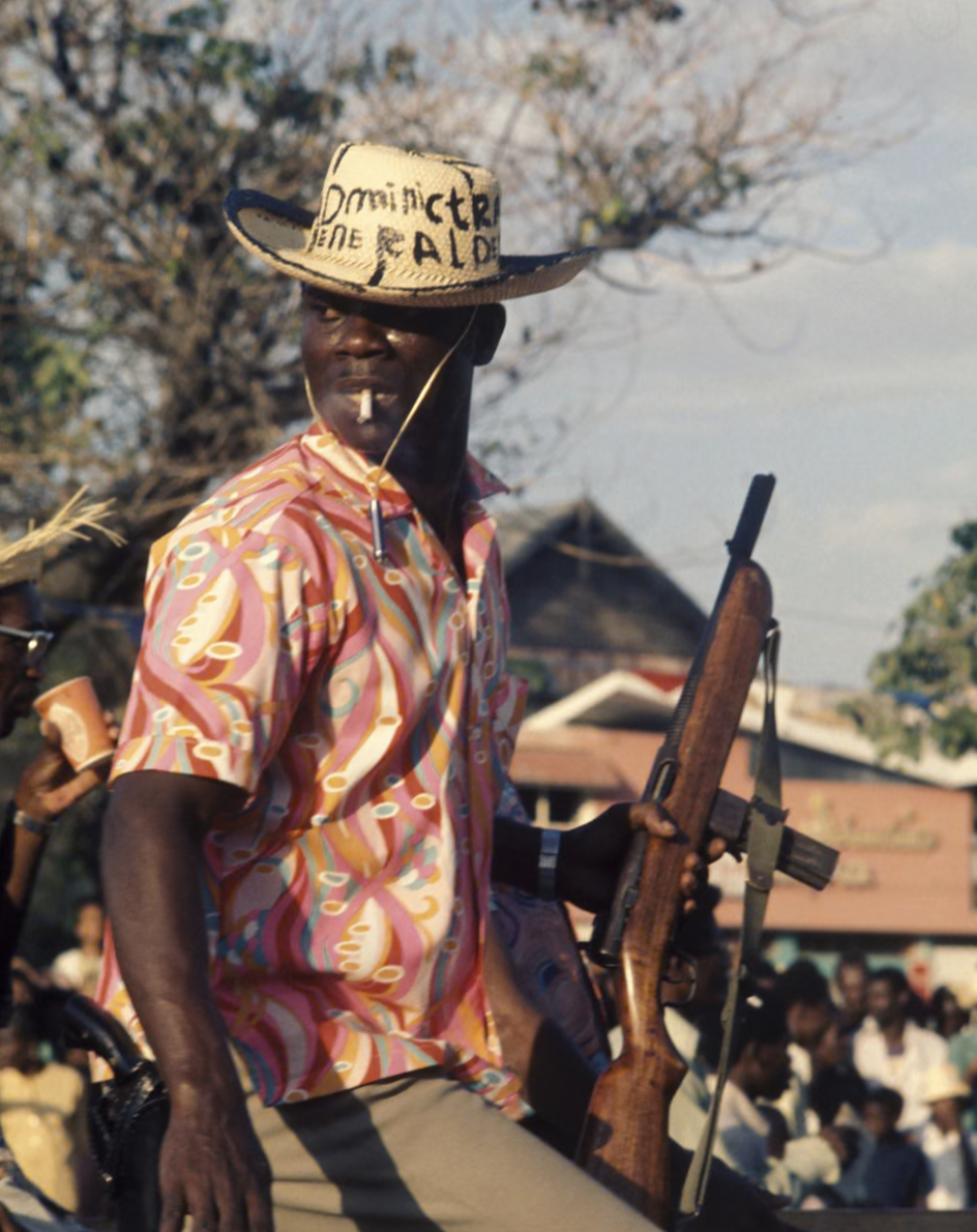 An armed Tonton Macoute patrolling the streets of Port-au-Prince, Haiti (1980) [Photograph]. In 100 years of photography in the Caribbean in pictures. The Guardian.