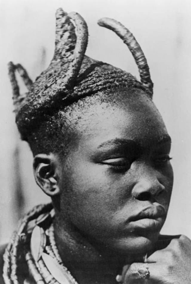 Married Ova Wambo woman wearing the Omhatela headdress, which resembles the horns of a bull. Photographed by A. Scherz in Namibia, (1940). Sourced from Vintag.es.