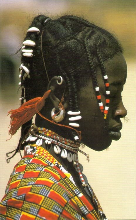 Fulani woman wearing traditional glass beads, cowrie shells, and silver adornments. The jewelry often signifies social class, tribe, or marital status.