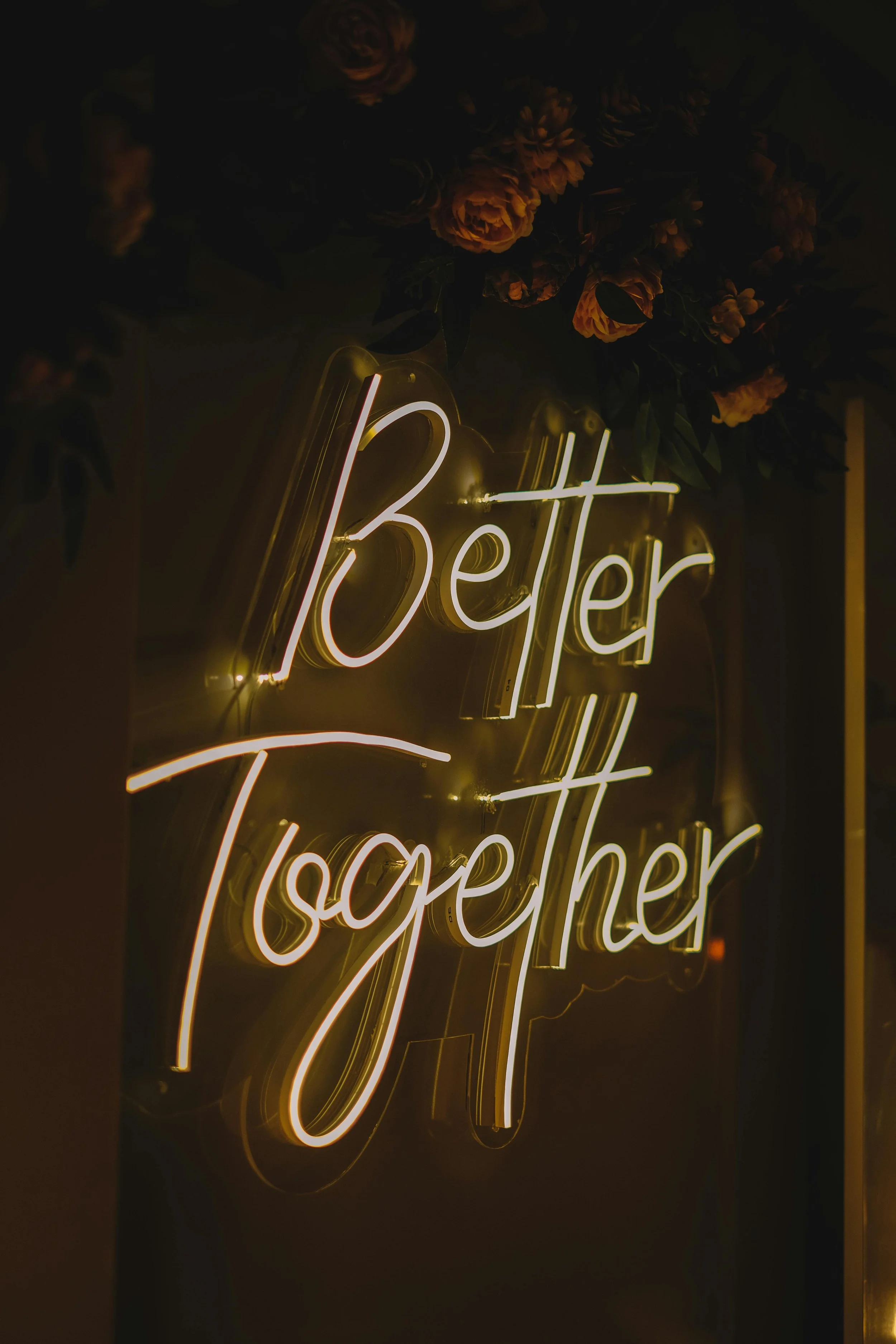 A neon sign reading 'Better Together' with floral decorations above it.