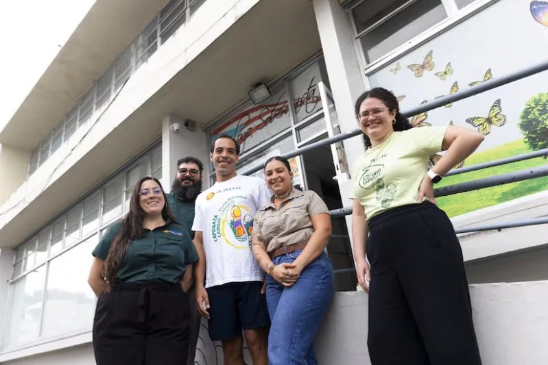 Five people smiling in front of a building with butterfly decorations on the windows.