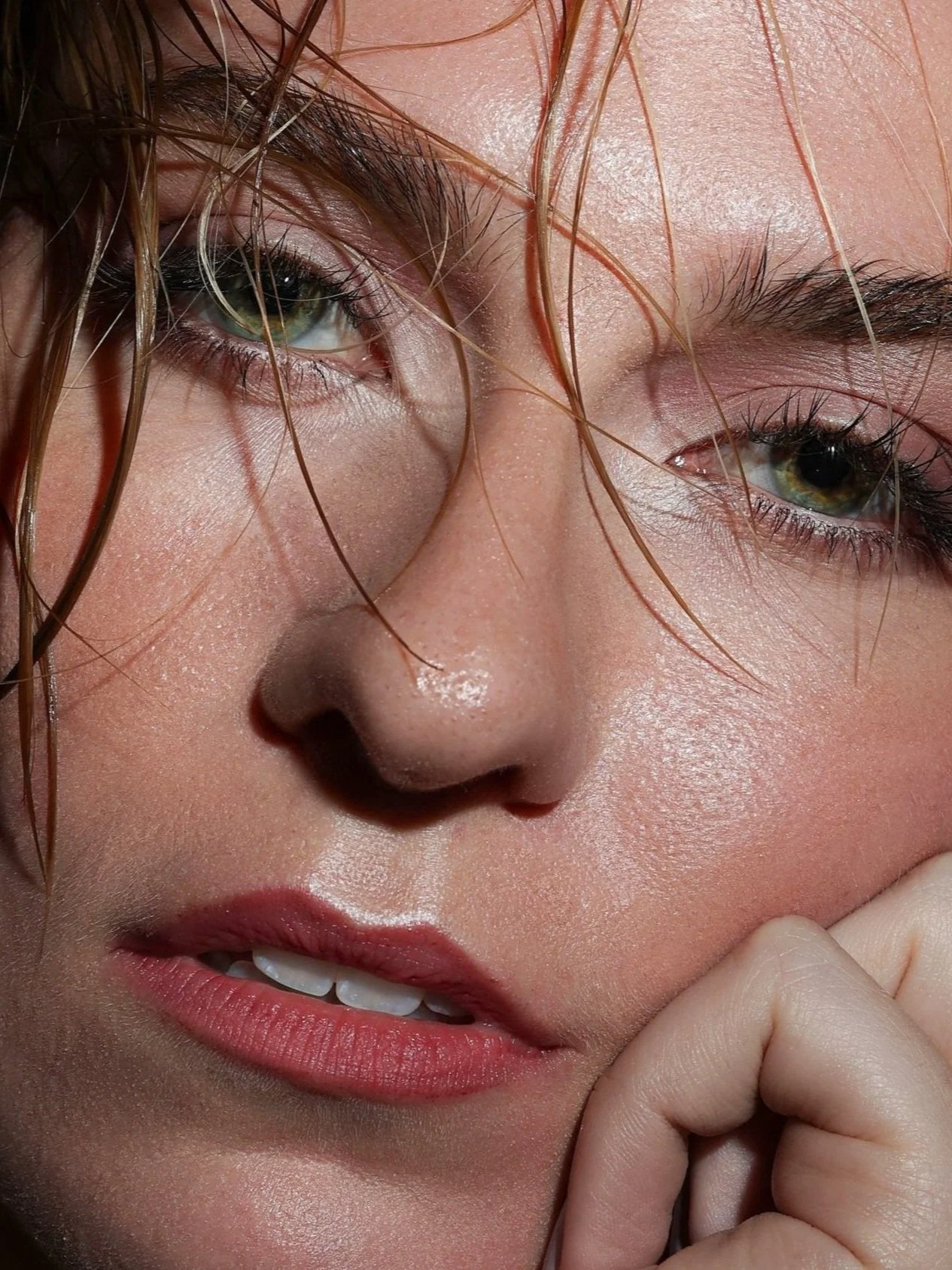 Close-up of a woman's face with green eyes, wet hair, and slightly parted lips.
