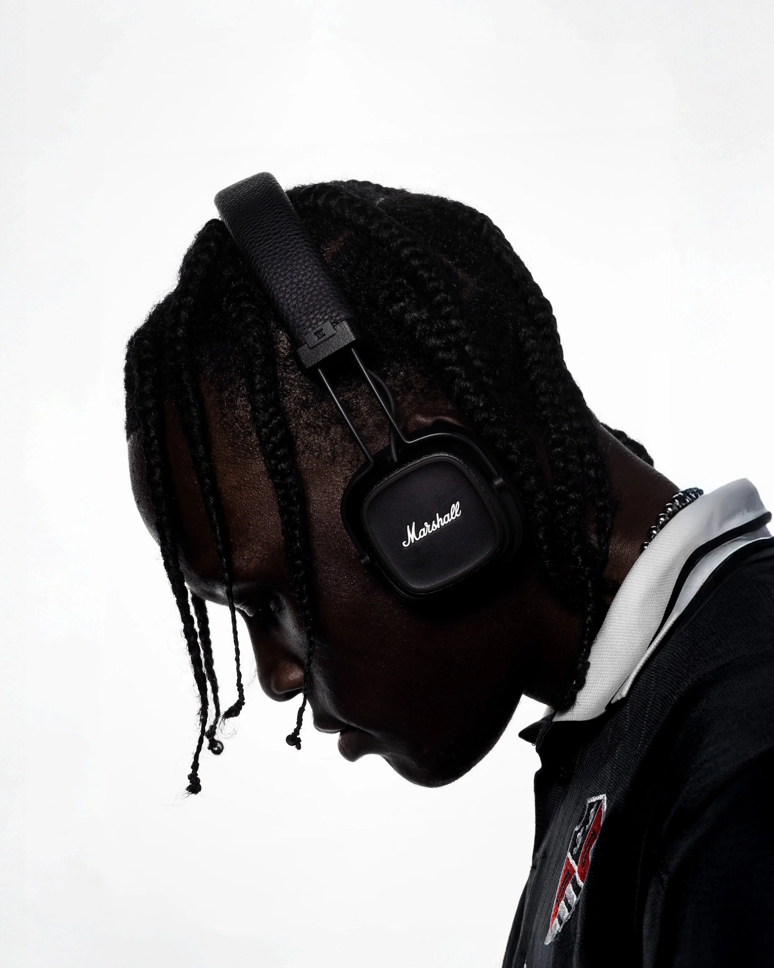 Side profile of a person with braided hair wearing black Marshall headphones against a plain white background.