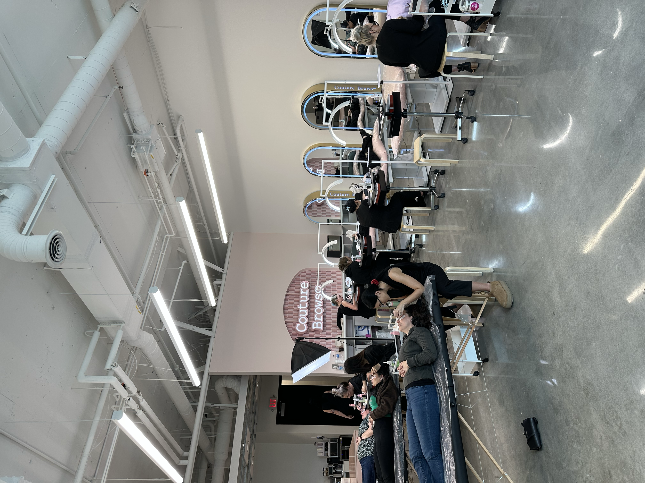 Beauty salon with multiple manicure stations, clients receiving nail services, and employees working on customers' nails.