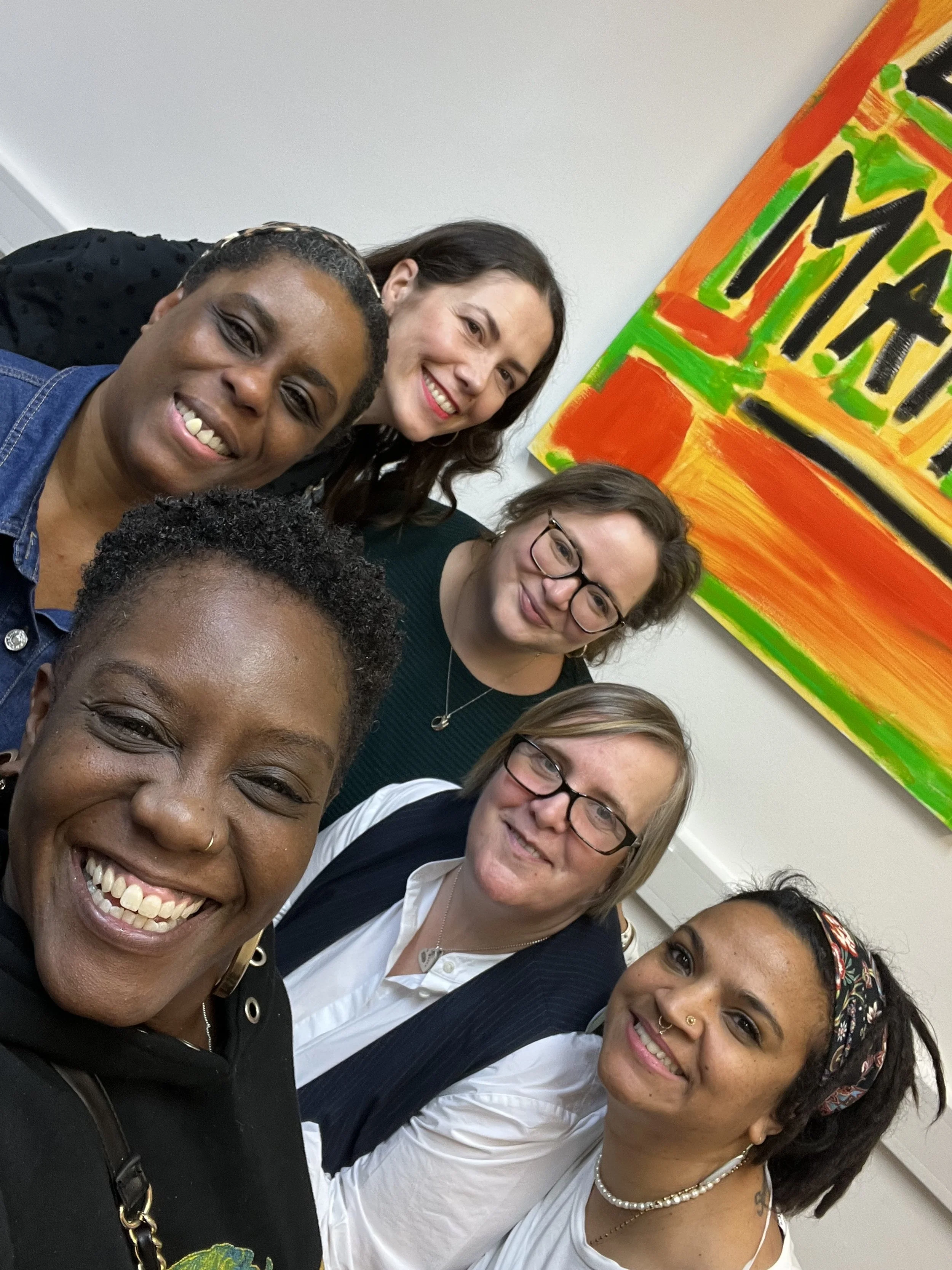 Group of six diverse women smiling and posing for a selfie in front of a colorful 'MARCH' sign.