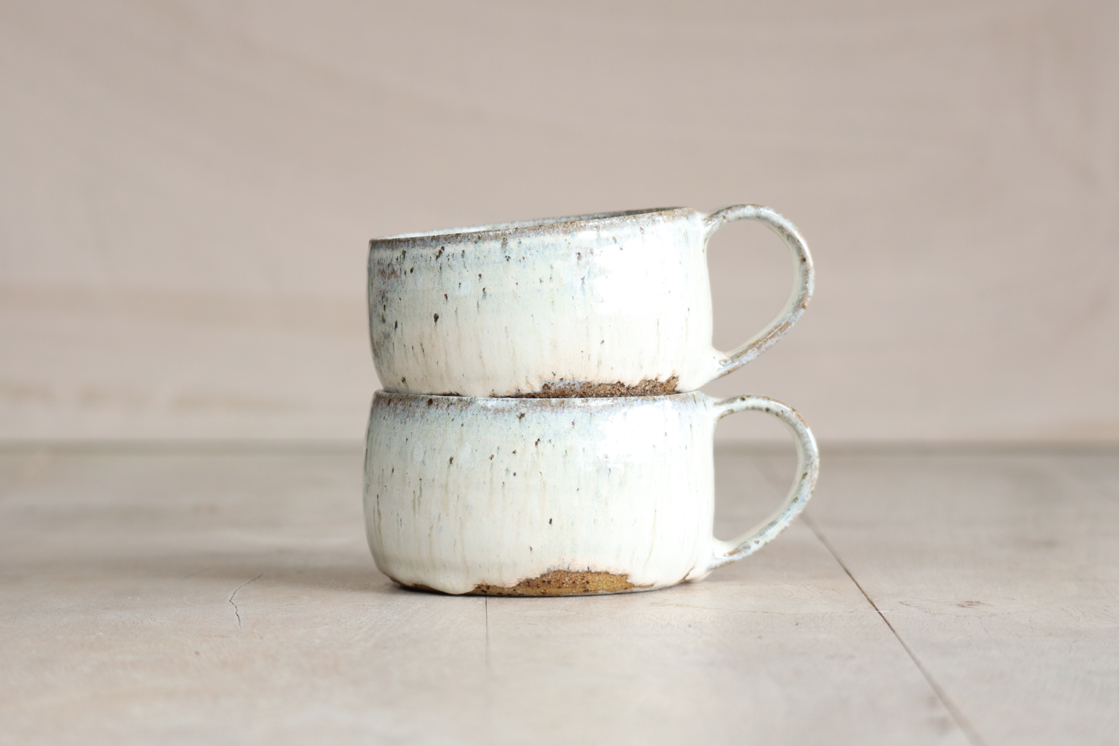 Two stacked vintage ceramic cups with a rustic, distressed cream finish on a light-colored surface against a neutral background.