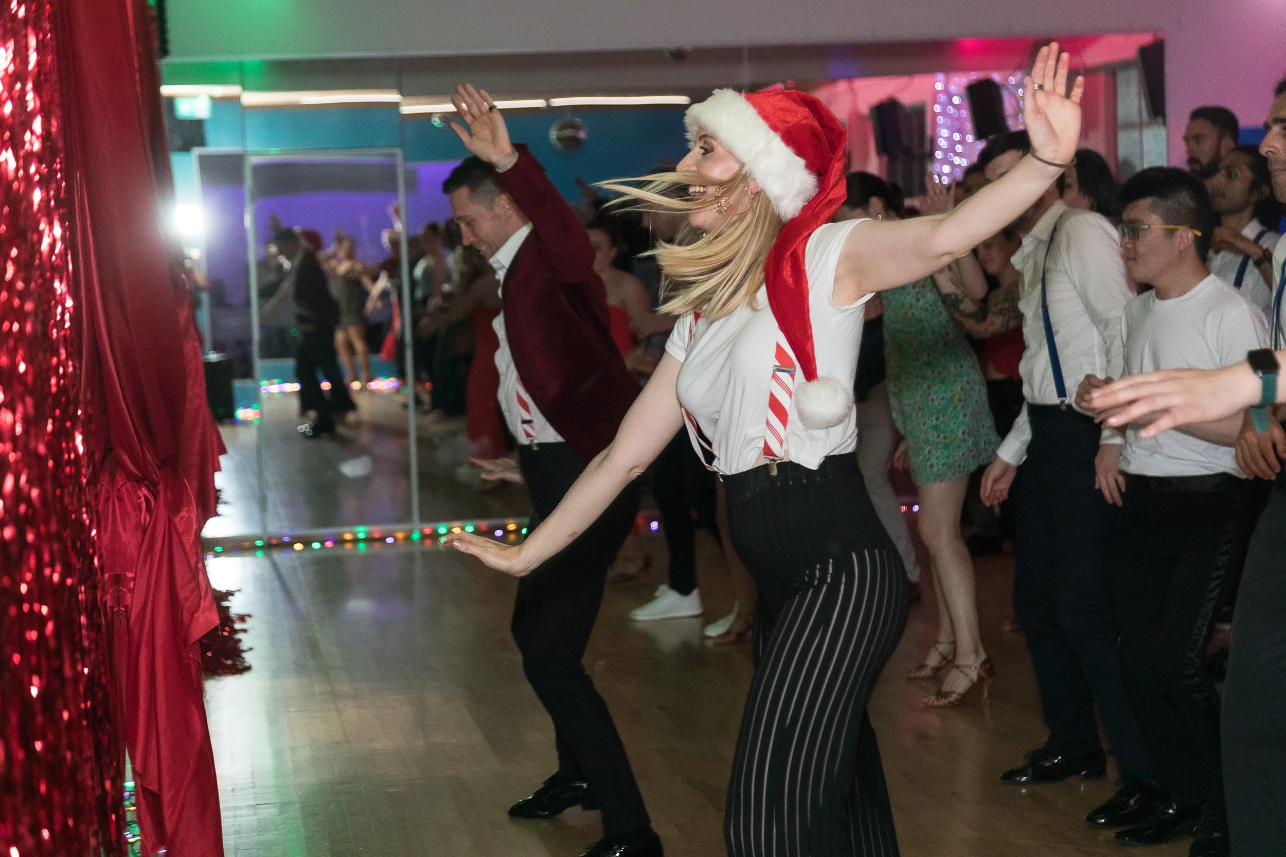People dancing at a holiday party, with a woman wearing a Santa hat in the foreground.