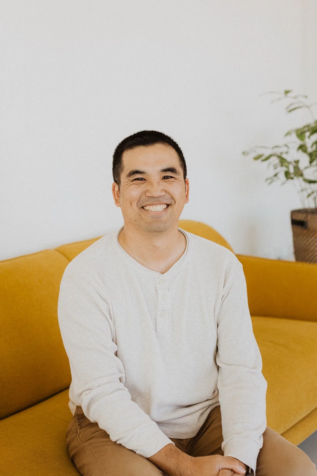 A man with glasses smiling, wearing a light blue checkered shirt, outdoors with blurred urban background.