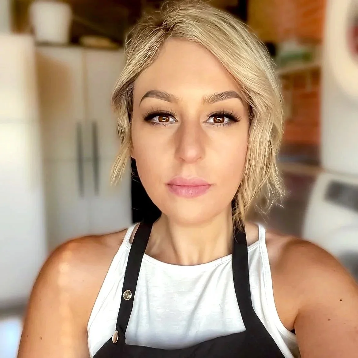 A woman with blonde hair, wearing a white sleeveless top