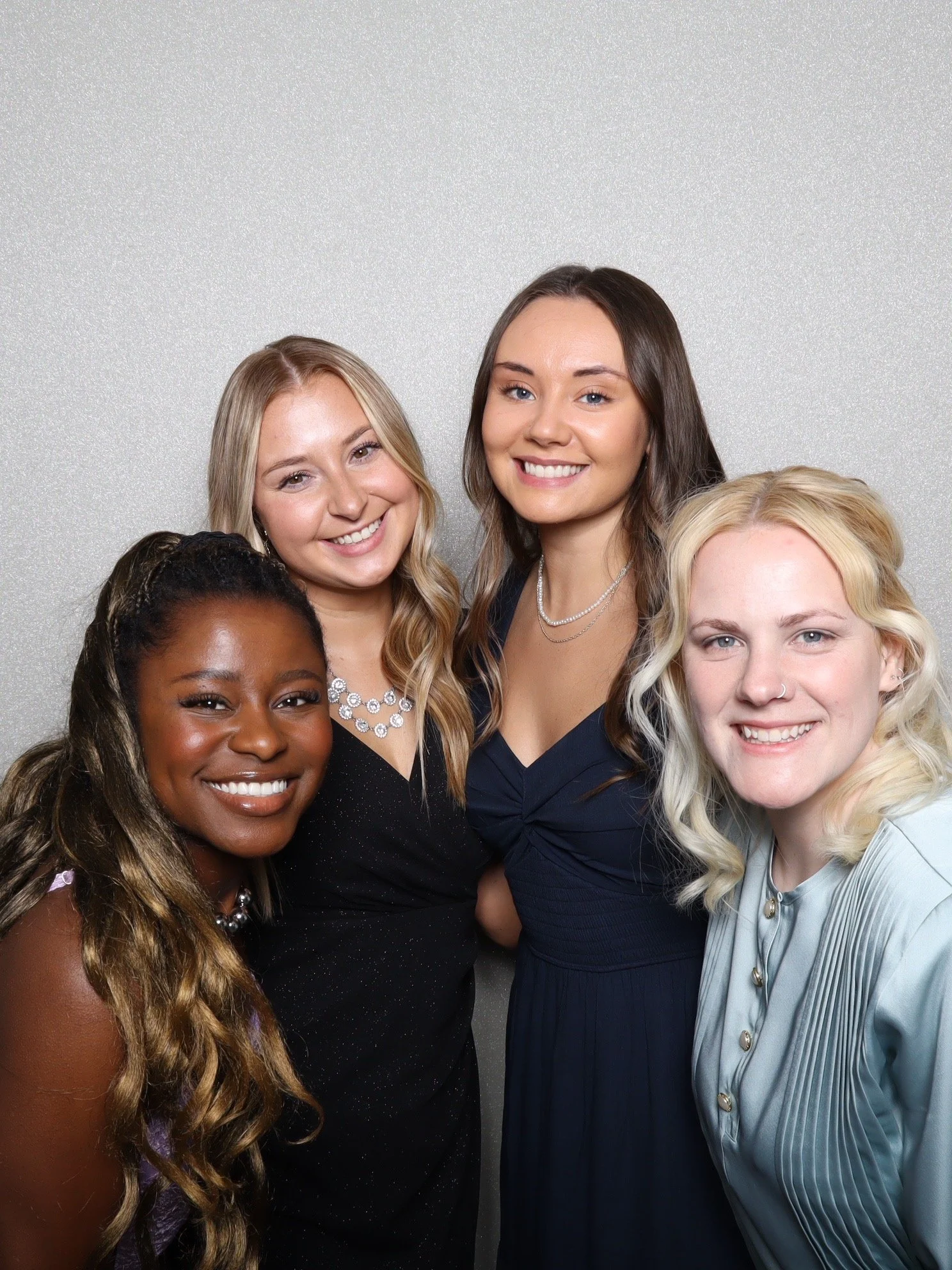 Group of five women smiling and posing close together in a photo booth against a plain gray background.