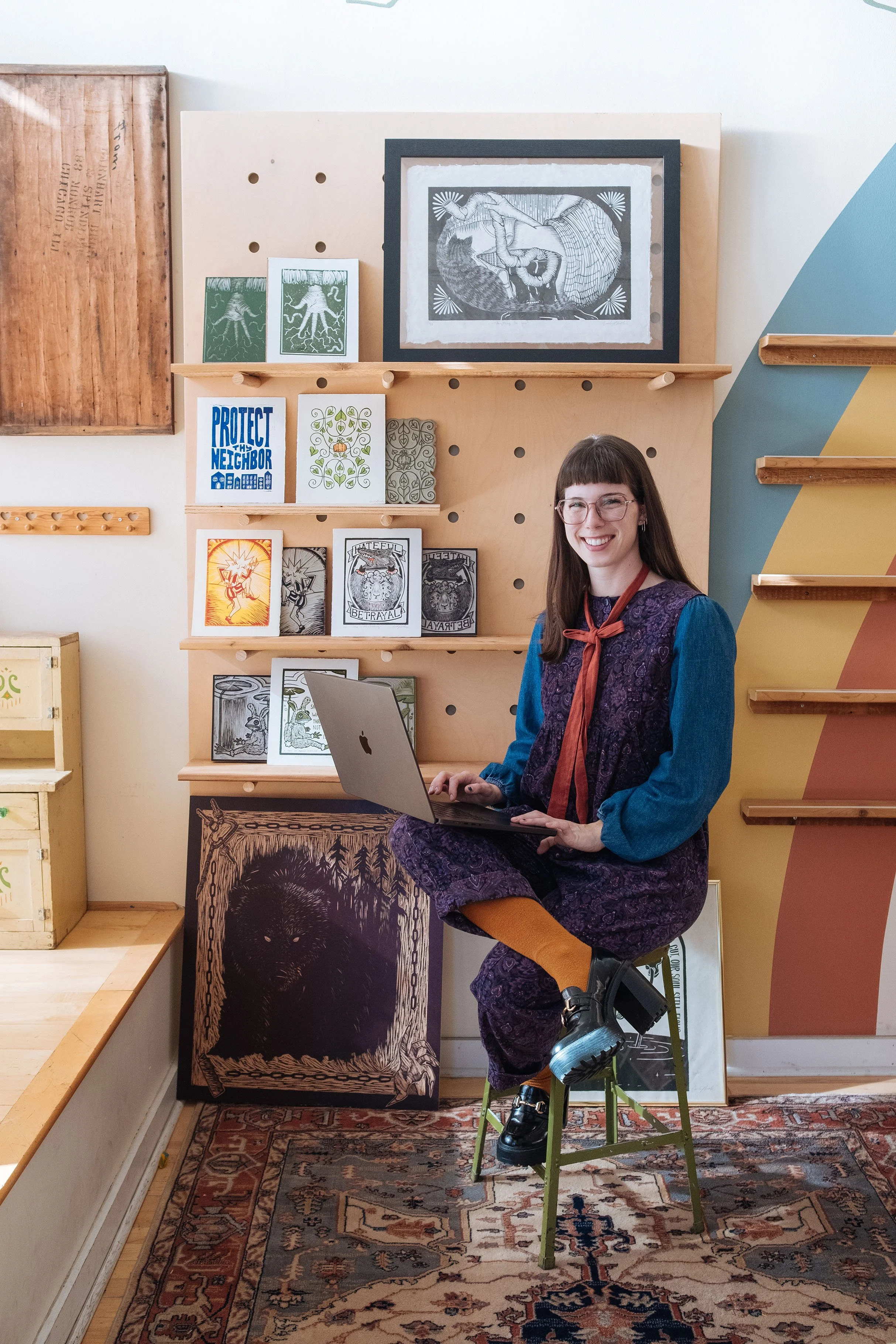 Photo of Emily smiling with her laptop and some of her art in the background