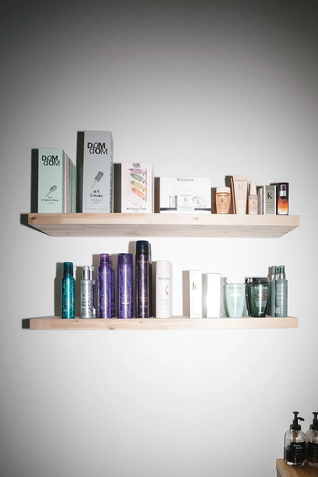 Two wooden shelves mounted on a wall displaying various hair and skincare products, including shampoos, conditioners, and treatments.