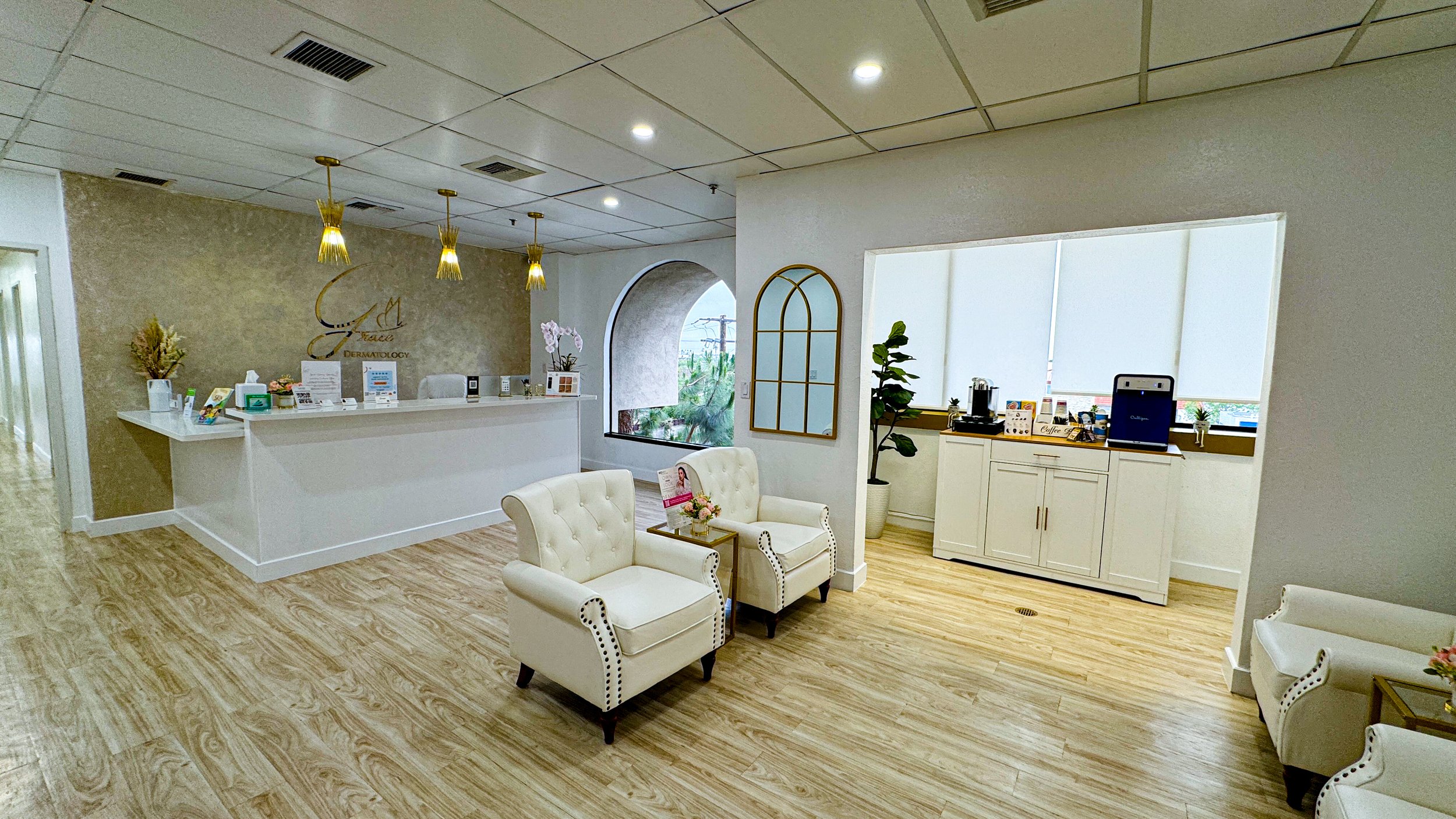 Grace Dermatology reception area with white front desk, cream armchairs, and gold pendant lighting
