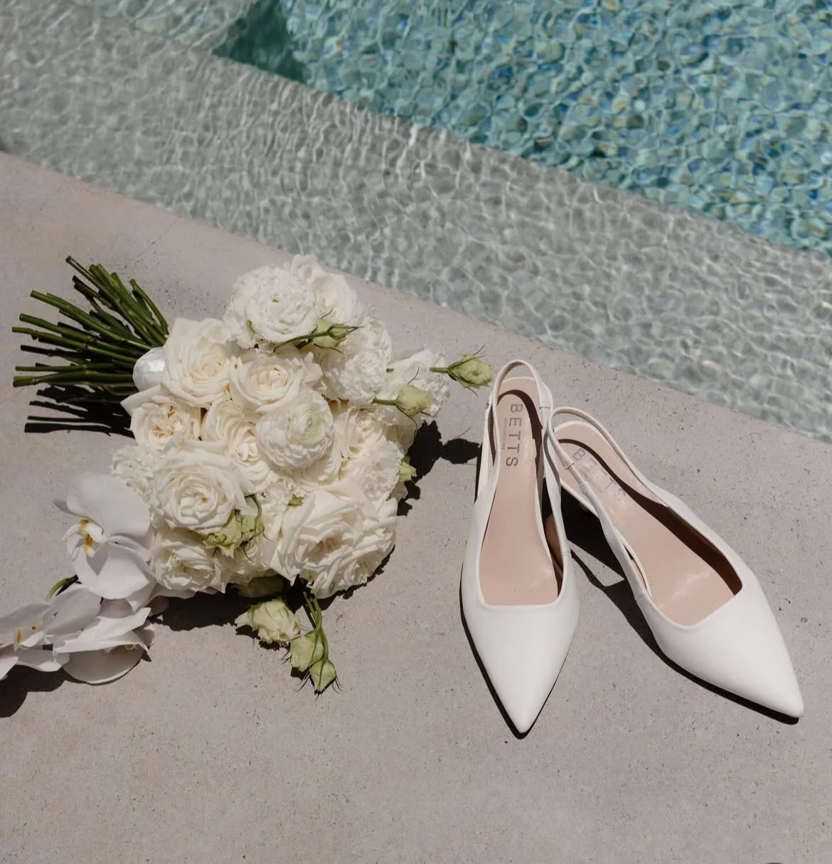 White wedding bouquet and shoes by a swimming pool.