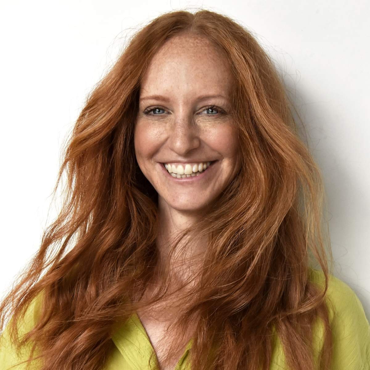 A woman with long, curly red hair smiling against a white background