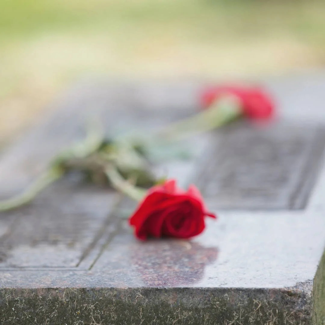 A single red rose lying on a headstone — symbolising love, remembrance, and the essence of a Rest in Peace message.