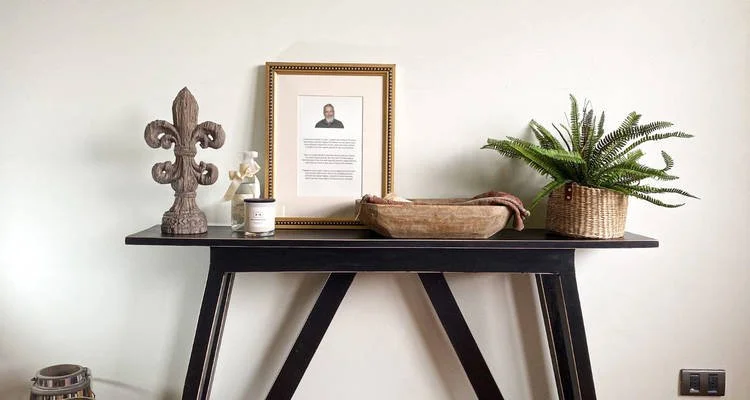 Memorial display table featuring a framed tribute, candle, wooden decor, and a basket of keepsakes.