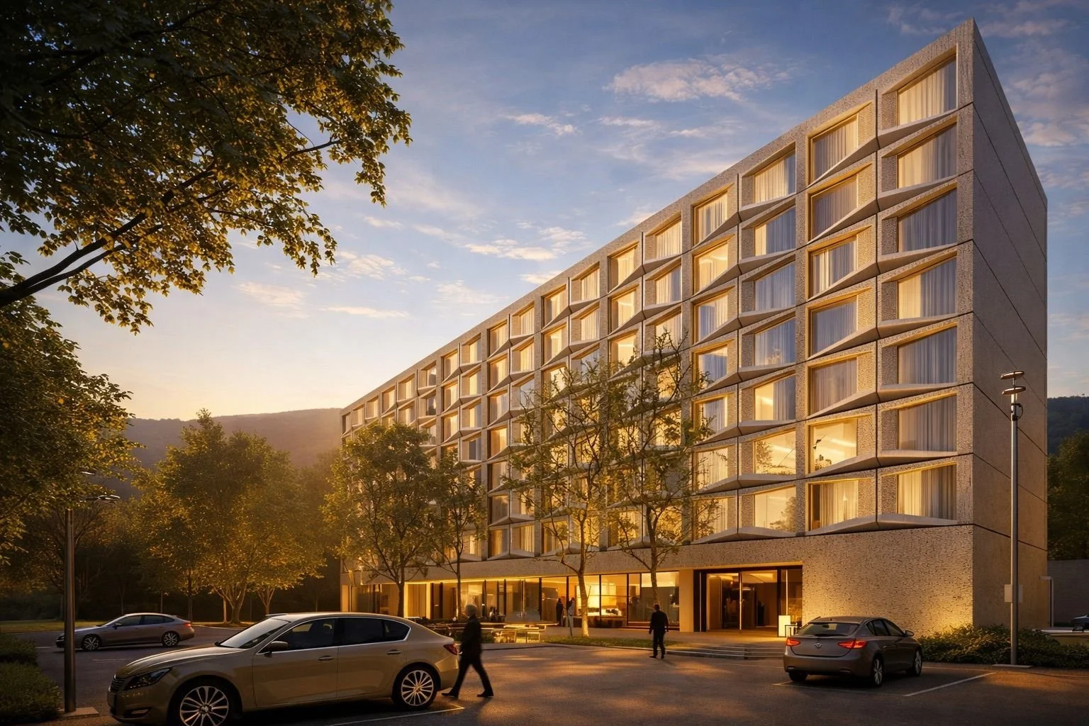 Modern hotel building at sunset with parking lot, trees, and people walking.