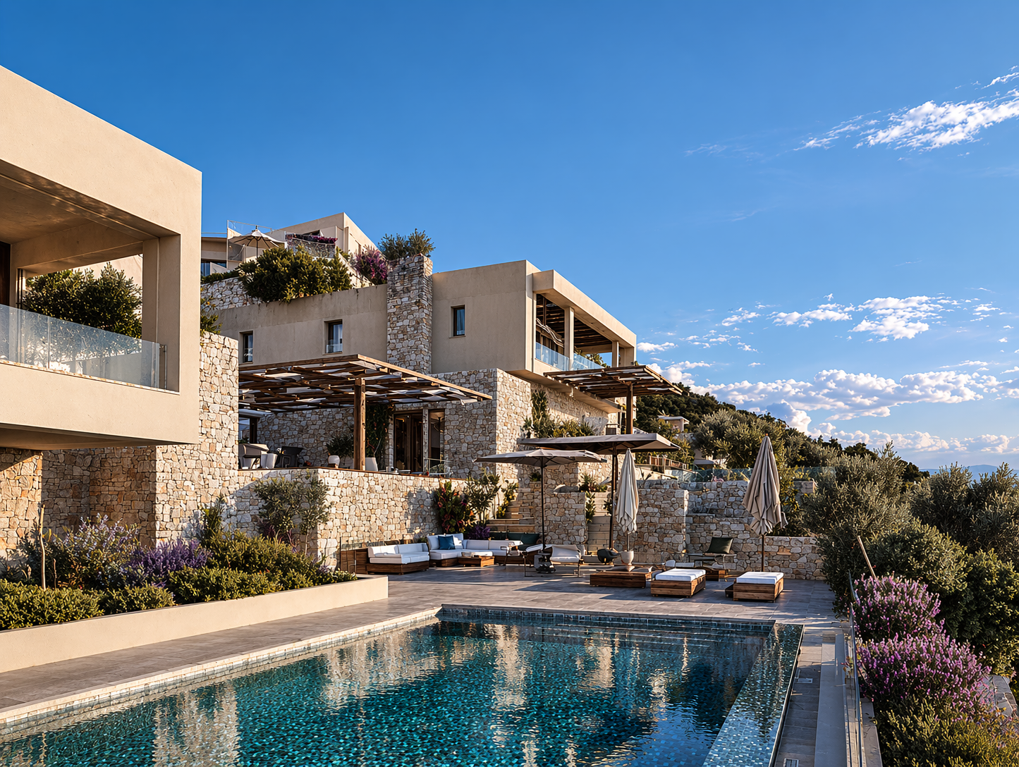 Luxury modern villa with stone and white plaster walls, outdoor pool, and a patio with lounge chairs and umbrellas, surrounded by greenery under a bright blue sky.