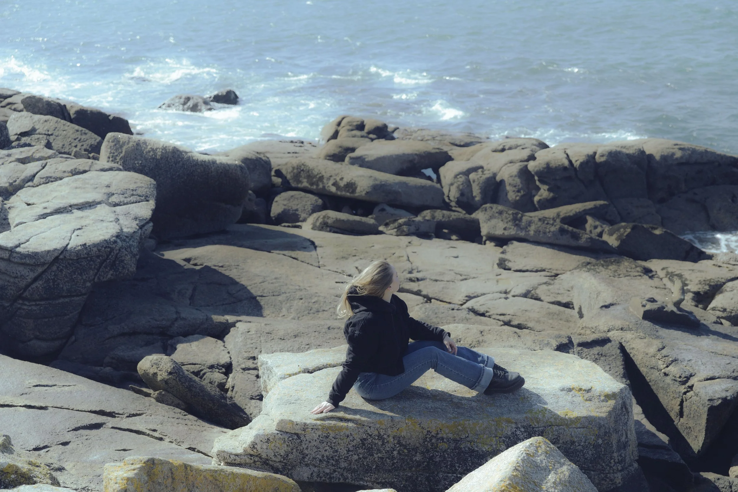 Donna seduta su una grande roccia sulla spiaggia con il mare sullo sfondo.