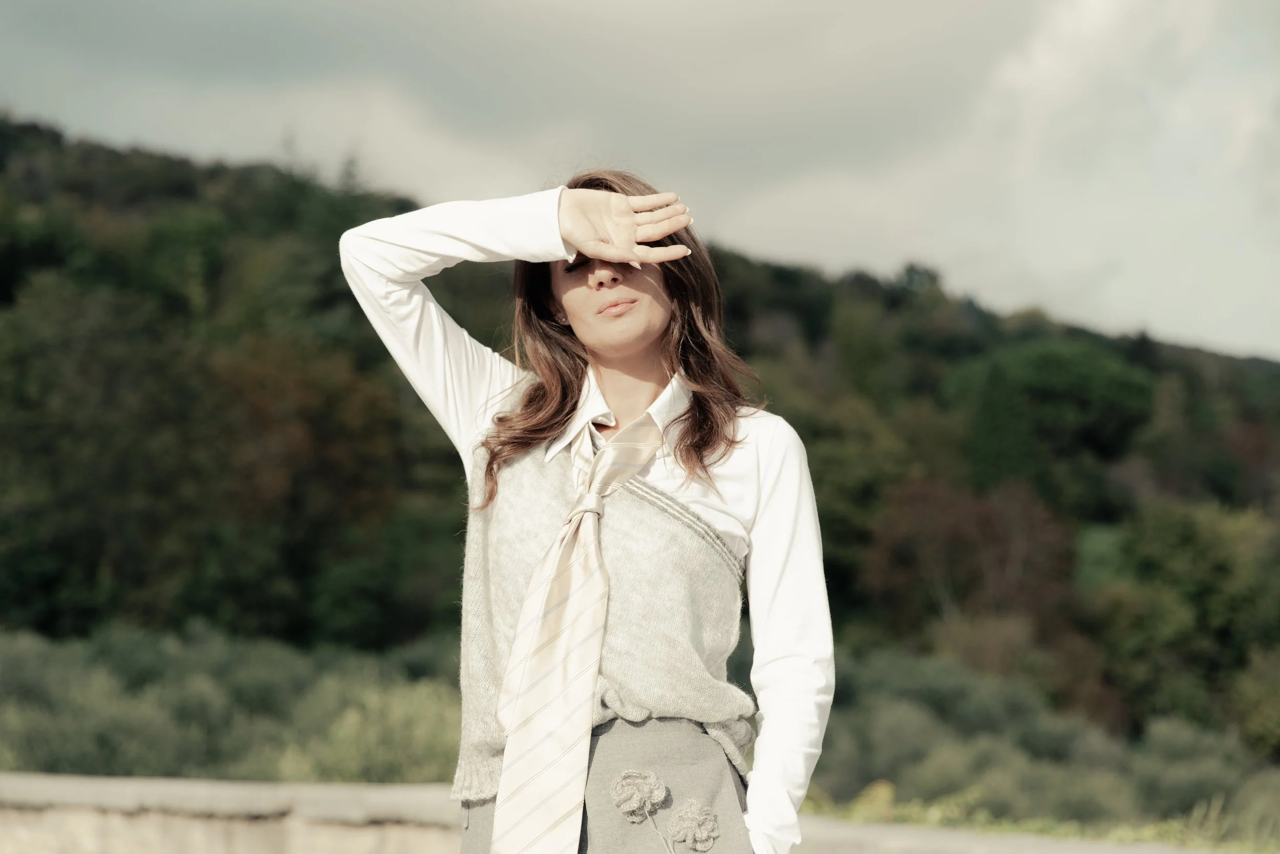 Una donna che si protegge dal sole con la mano sulla fronte in un paesaggio naturale con colline e alberi