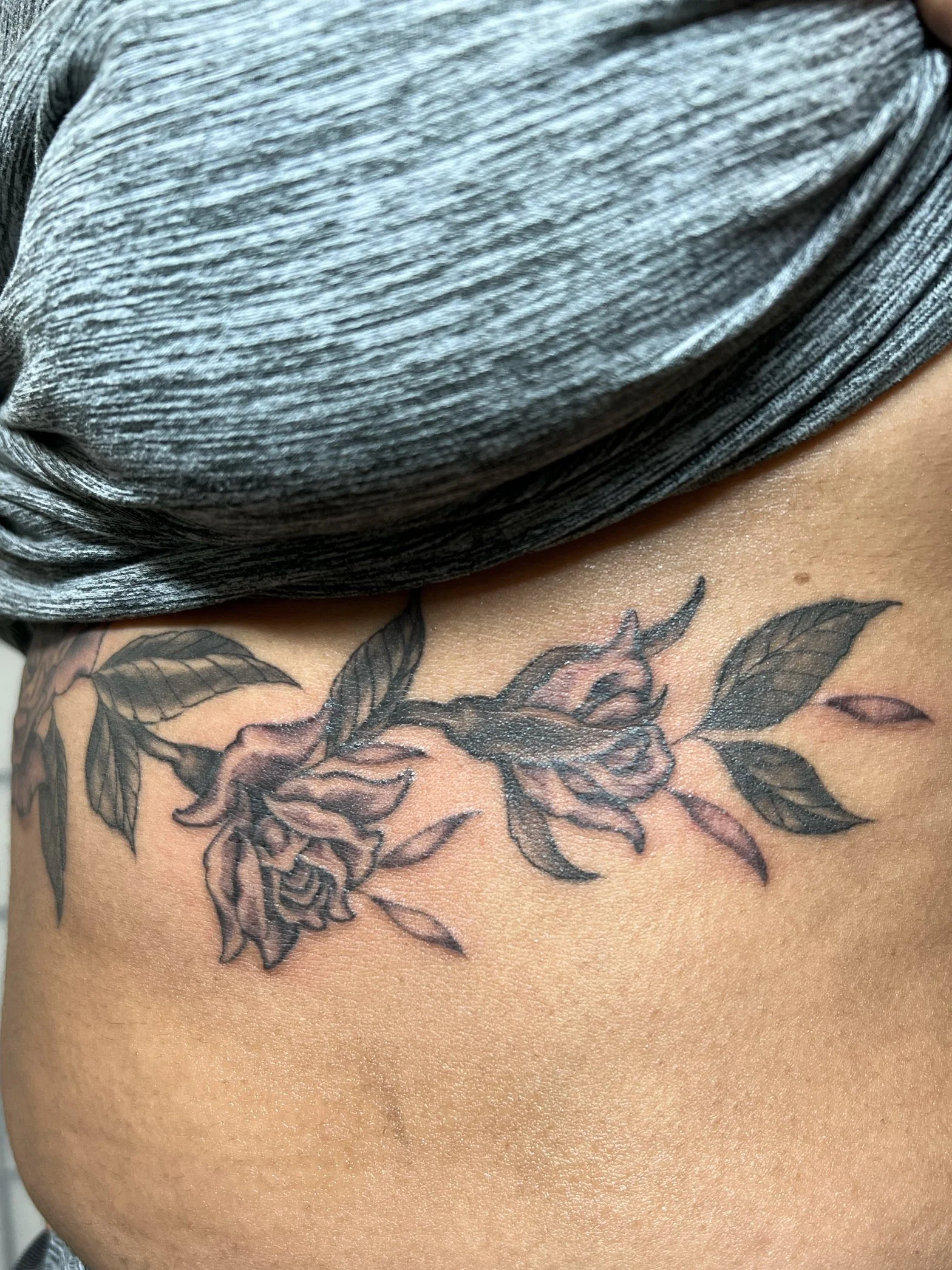 Delicate and fine line tattooed of a rose garland, on the sternum and ribs and bra line for a feminine look by Harriet Street in Brighton, UK