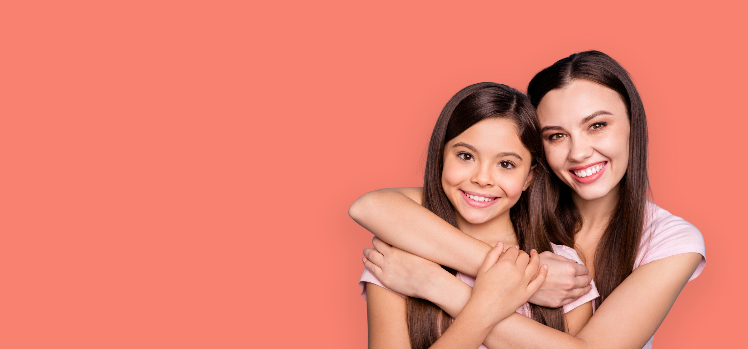 Une mère et sa fille souriantes qui se font un câlin devant un fond rose