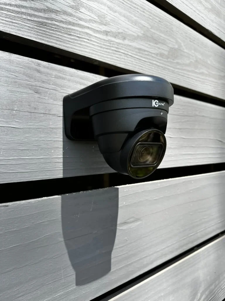 A black security camera mounted on a gray wooden wall.