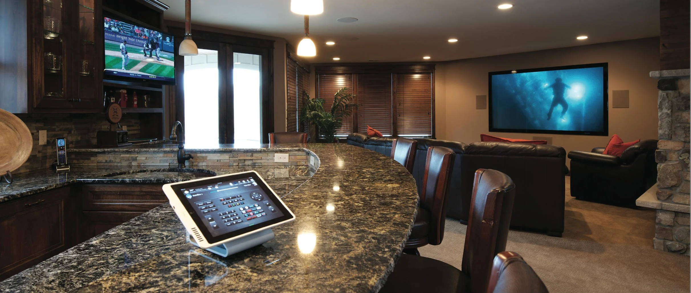 Luxury home theater with bar counter, touchscreen control, large TV screens, leather seating, and stone accents.