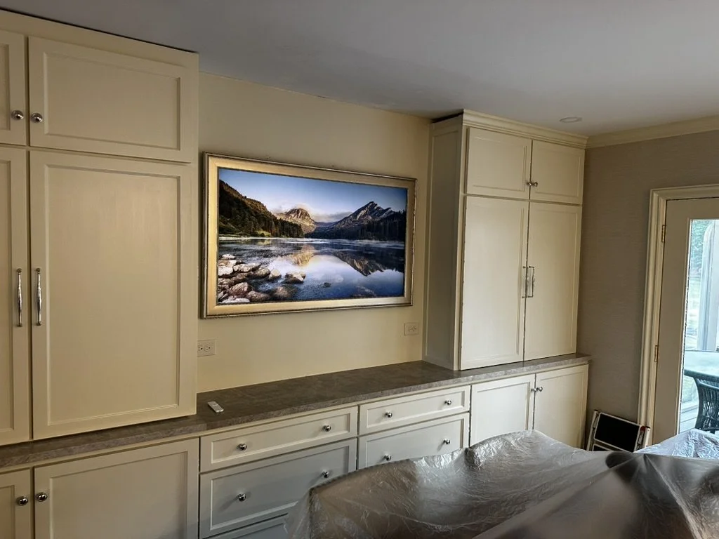 Living room with built-in cream-colored cabinets, a landscape painting of a river and mountains, and a glass door leading outside.