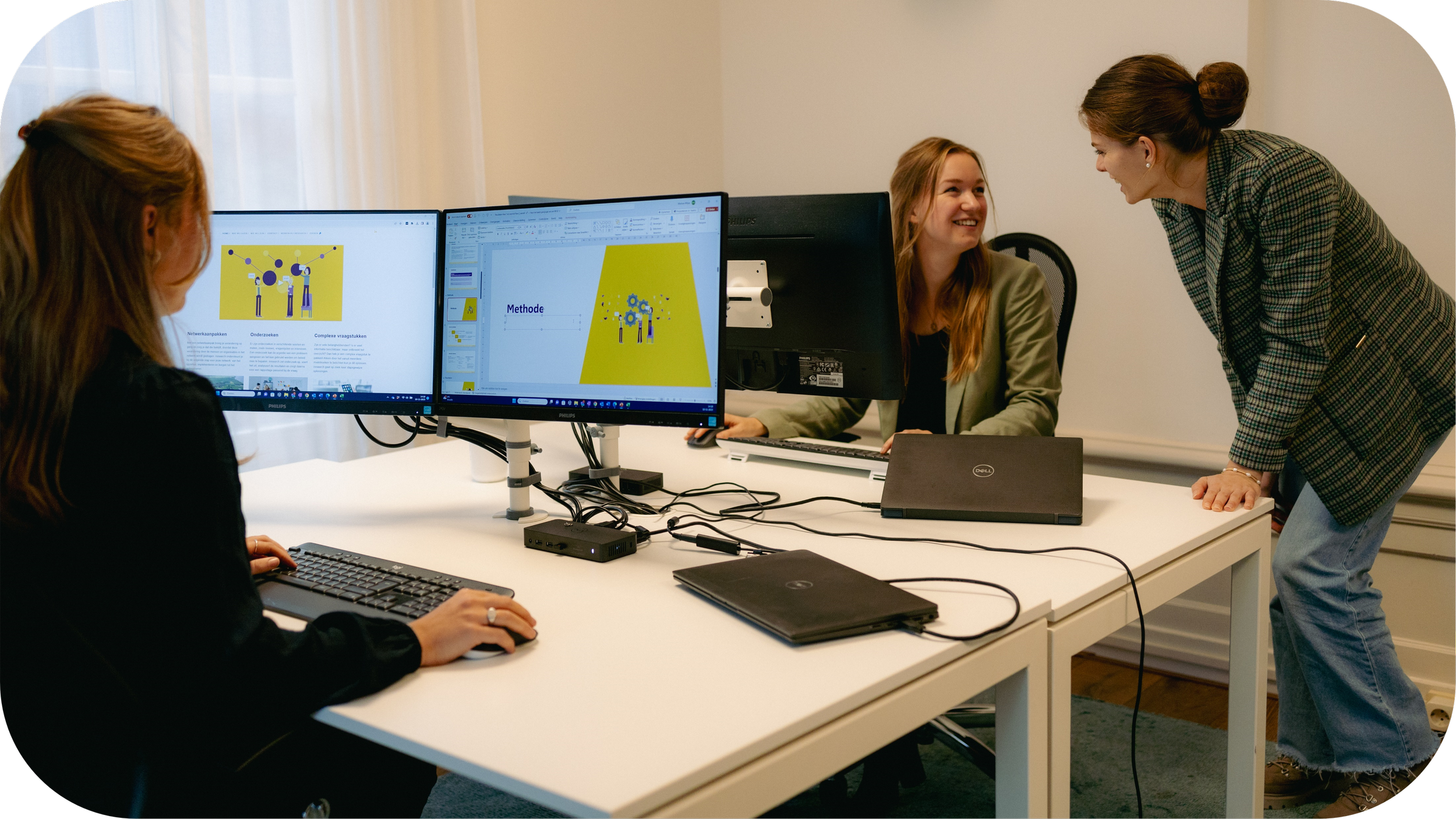 Sfeerfoto van het kantoor van iresearch met een collega die achter de computer zit te werken en twee andere collega's die met elkaar praten achter een andere computer