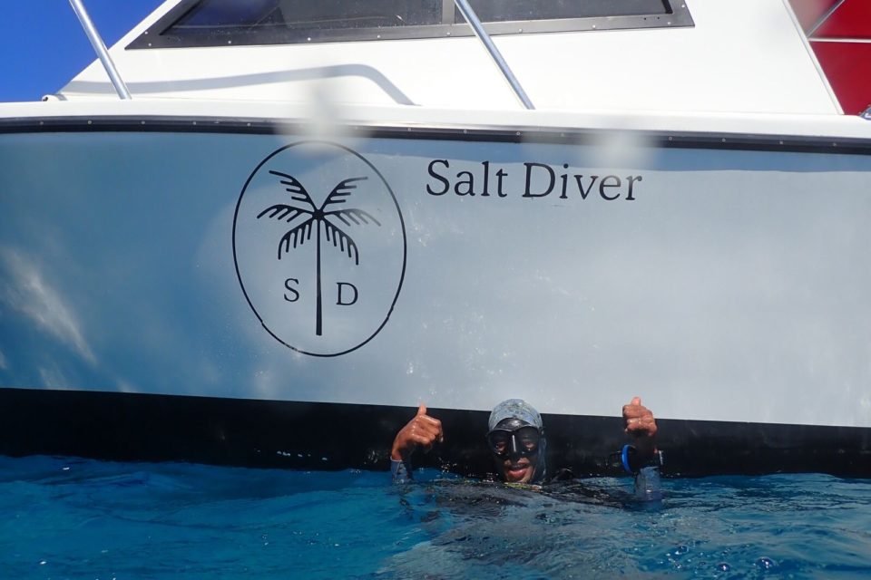 Scuba diver near boat with 'Salt Diver' logo on hull in ocean.