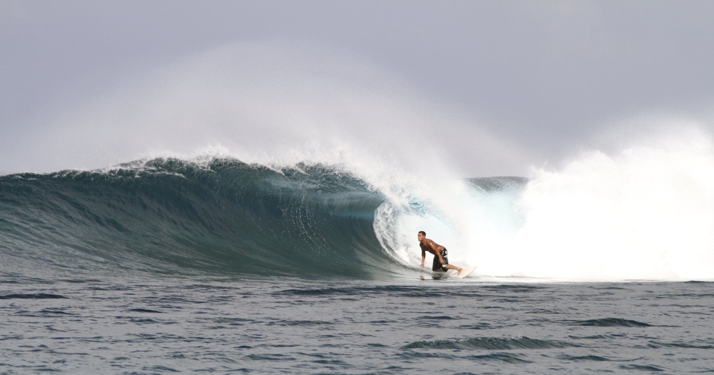 Surfer riding a large ocean wave, mid-motion, with a curling wave formation in the background.