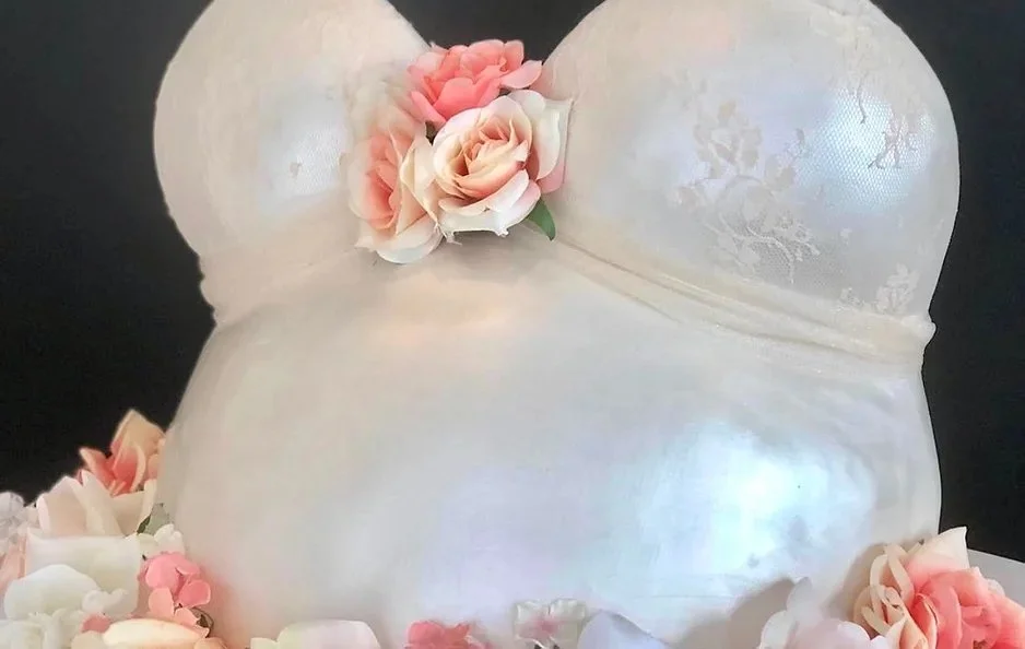 A cake decorated to look like a white bra with pink and white flowers adorning it.