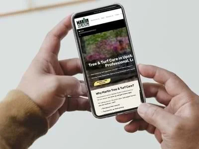 Person holding a smartphone displaying Martin Tree and Turf Care’s website quote request page, showing tree and turf care services in Upstate South Carolina.