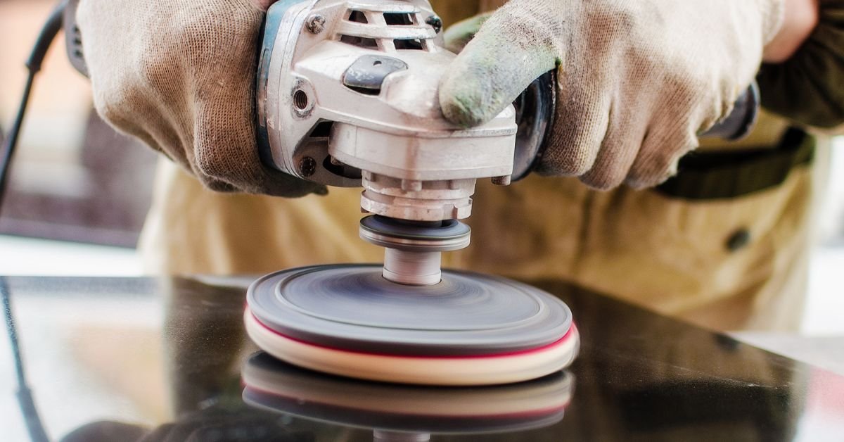 A close-up of a person with gloves holding a grinder to the surface of a black stone slab to polish