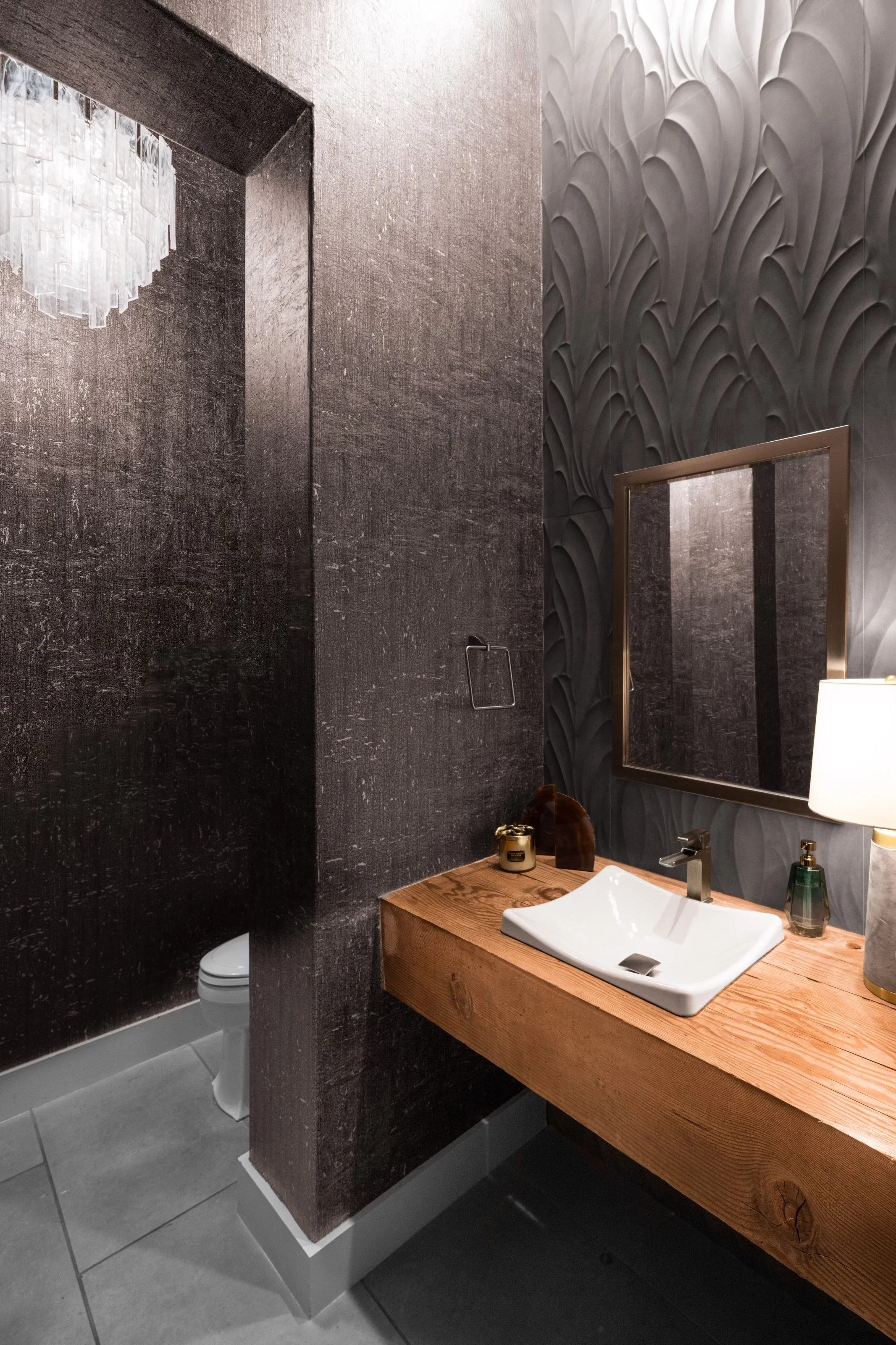 Modern bathroom with textured dark walls, wooden countertop, white sink, mirror, and toilet.