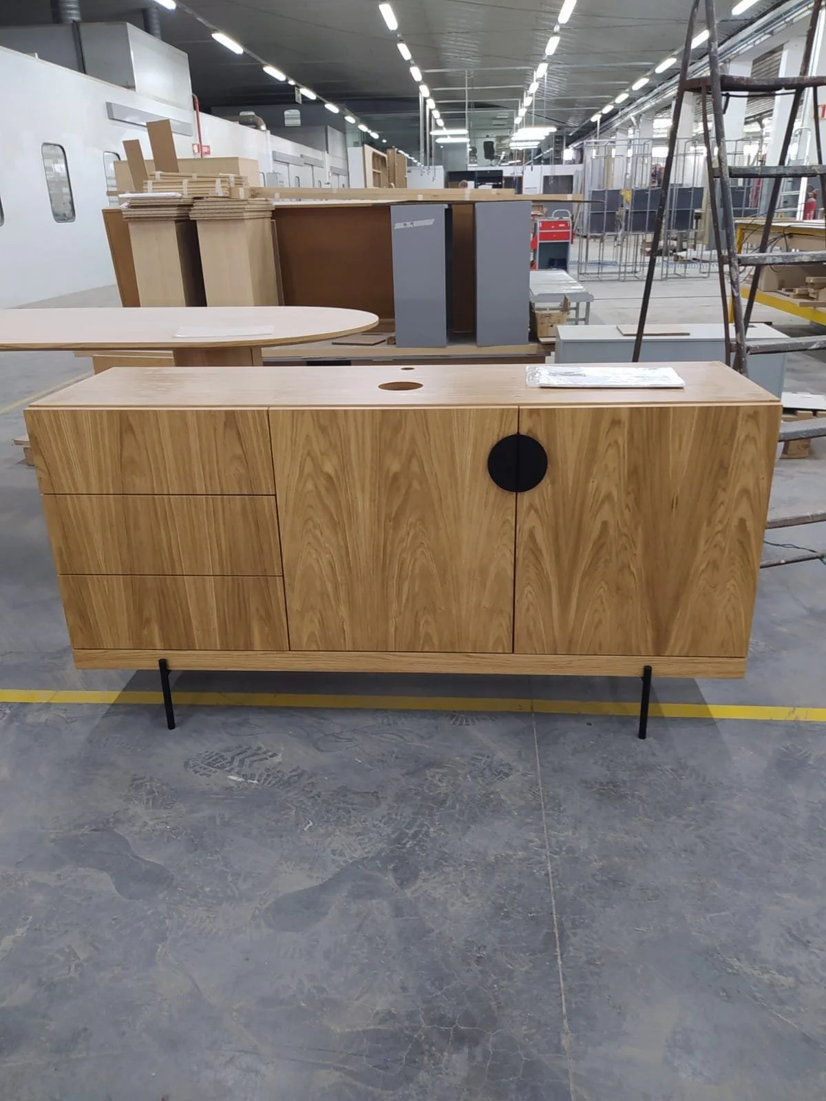 Un meuble en bois dans une usine ou un atelier de fabrication, avec portes et tiroirs, posé sur un sol en béton.
