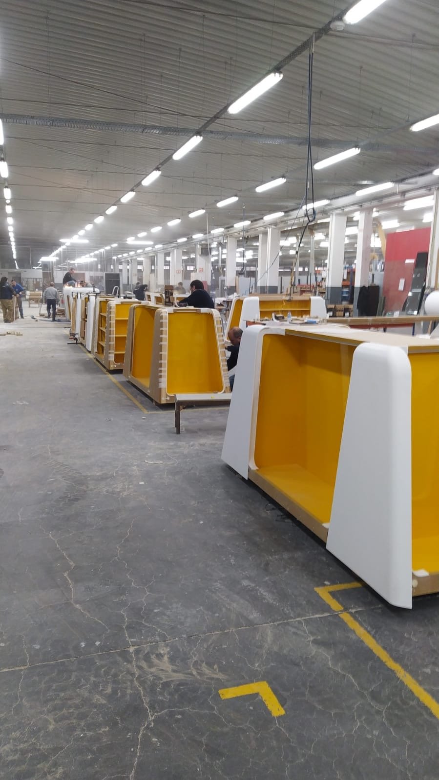 Une usine ou un atelier de fabrication avec des travailleurs assemblant des meubles ou des équipements colorés en jaune et blanc.