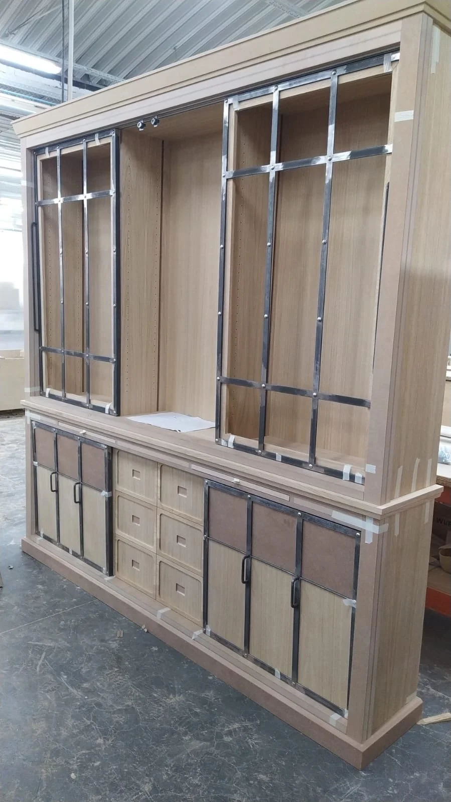 Une grande armoire en bois en cours d'assemblage dans un atelier, avec des cadres métalliques pour les portes.