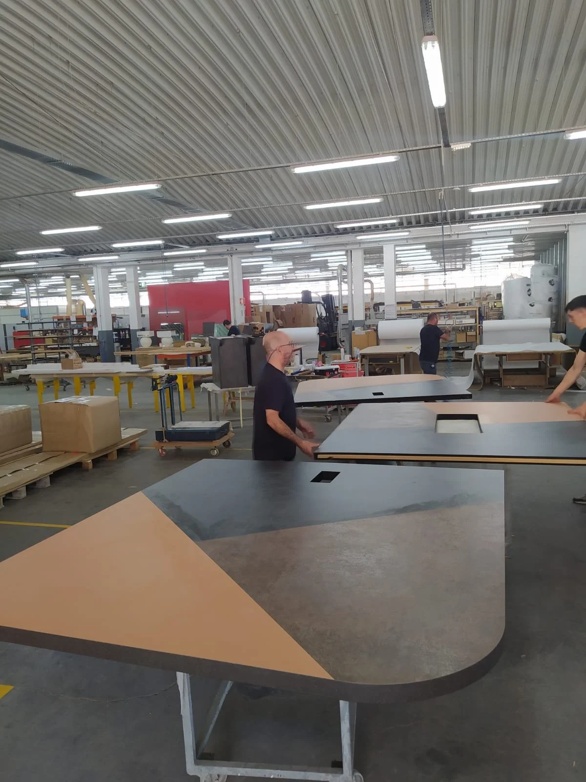 Une usine de fabrication de meubles avec plusieurs personnes assemblant et inspectant des tables, dans un espace industriel bien éclairé.