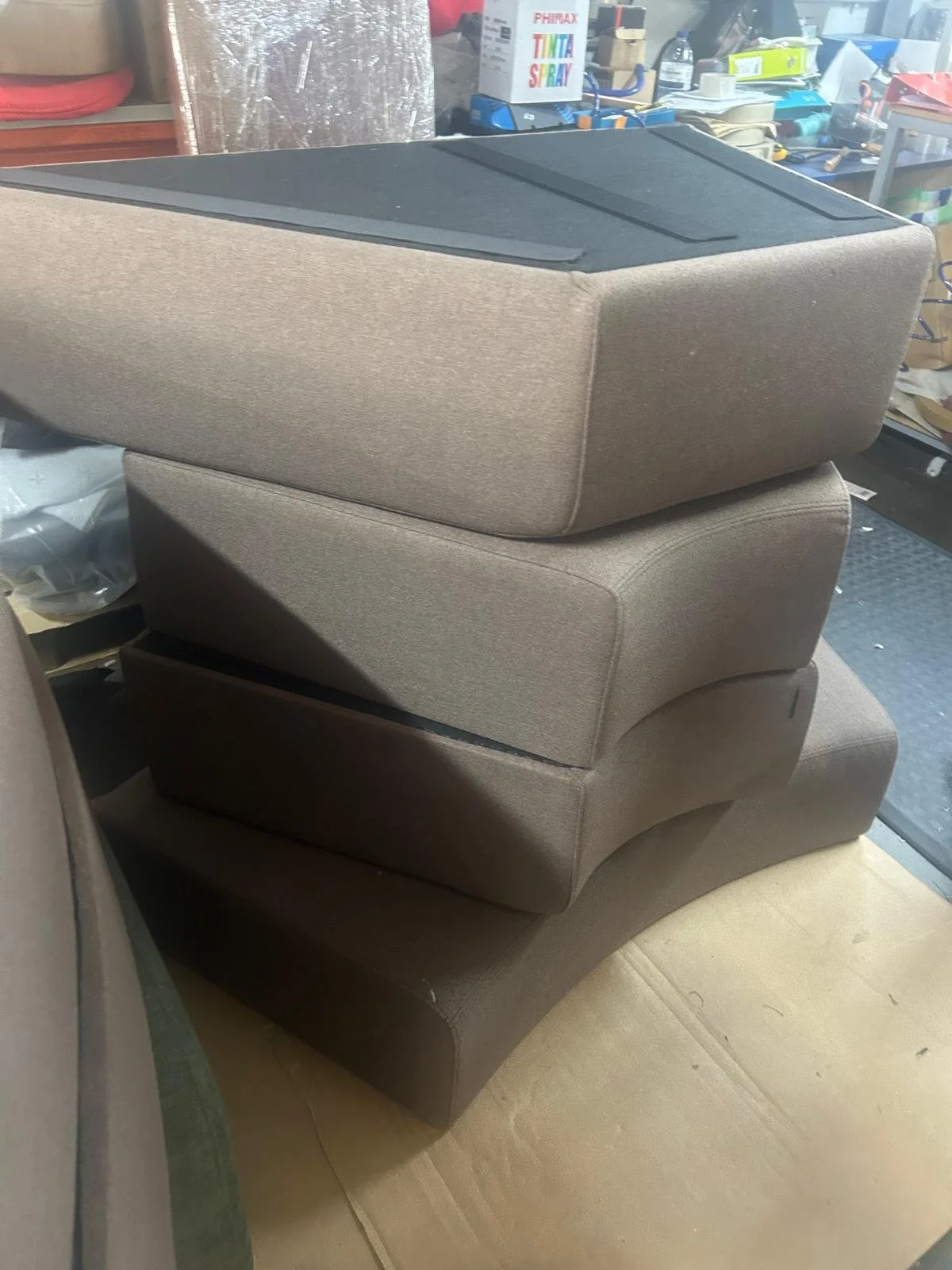 Une pile de quatre boîtiers audio ou enceintes de couleur beige, placés en zigzag, dans un environnement de bricolage ou de stockage